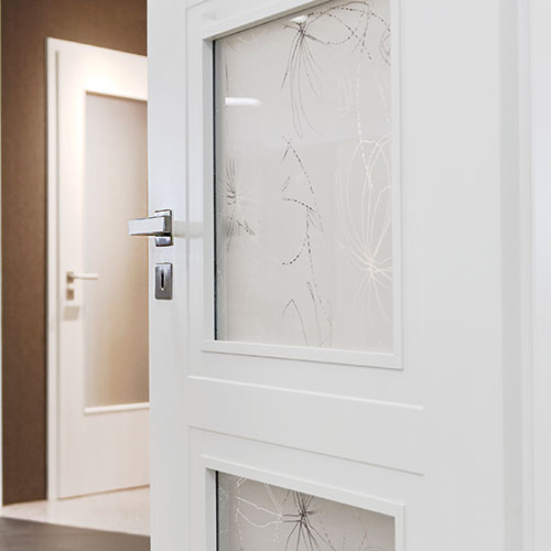 Eine weiß lackierte Zimmertür mit gemustertem Glaseinsatz steht offen und gibt den Blick auf eine weitere weiße Zimmertür frei. Diese Tür ist Teil unserer Türenausstellung in Hildesheim.